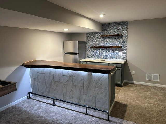 Finished basement with marble bar, wood countertop, stone accent wall, and kitchenette