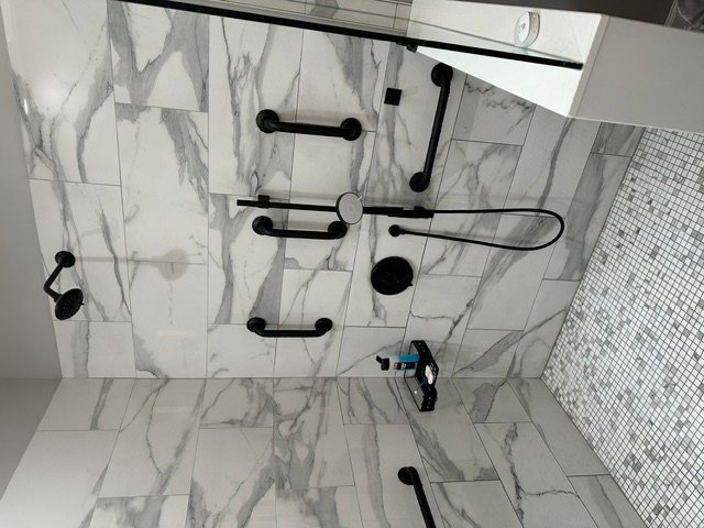 Marble-look tile bathroom with black hardware fixtures and mosaic tile accents