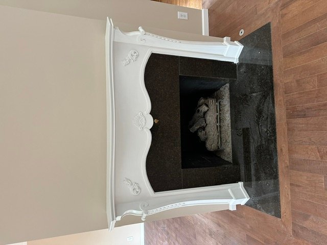 White decorative fireplace mantel with ornamental details and dark stone interior chamber