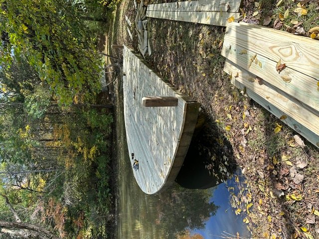 Wooden bridge with railings spanning over water in wooded setting